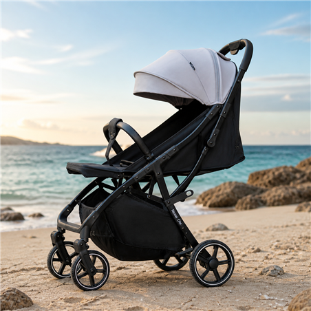 Black-frame baby stroller with gray canopy, reclining seat, four wheels and under-seat storage basket, parked on a sandy beach w